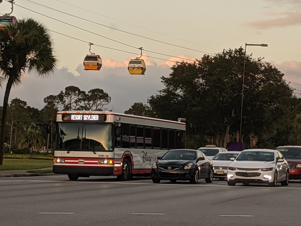 Walt Disney World Skyliner in the background as a Disney bus drives down the road